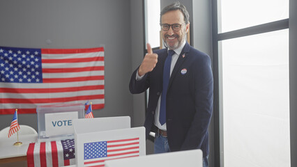 A bearded mature man with a thumbs up in an american electoral college setting adorned with flags.