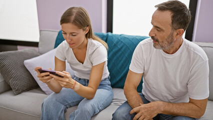 Father and daughter sitting on sofa using smartphone at home