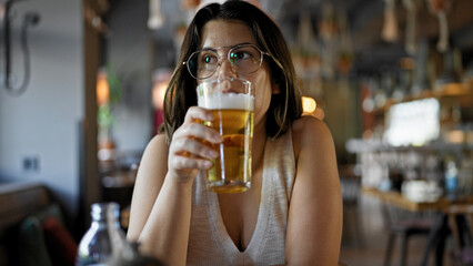 Young beautiful hispanic woman drinking beer at the restaurant