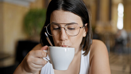 Young beautiful hispanic woman drinking coffee sitting on the table at cafeteria