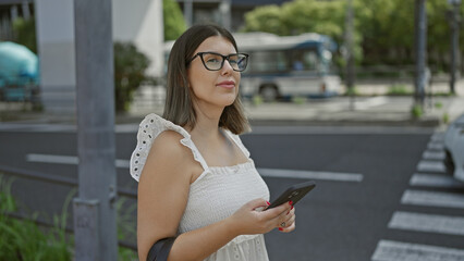 Fototapeta premium In the bustling streets of tokyo, a beautiful hispanic girl with glasses, a tech-savvy traveller, uses her phone app, anxiously waiting for her taxi ride.