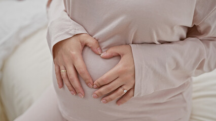 A pregnant woman lovingly holds her belly while standing in a softly lit bedroom setting, evoking warmth and maternity.