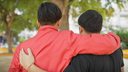Two asian men in friendship embrace outdoors, with greenery in a tranquil urban park setting