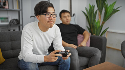 Two asian men enjoy gaming in a modern living room, reflecting leisure and friendship.