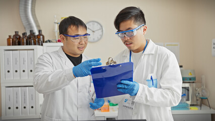 Two men in lab coats collaborate in a scientific laboratory, discussing over a clipboard.