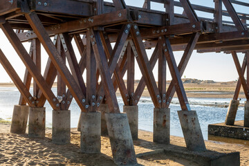Bottom of a walkway bridge to the beach with wooden beams in the Atlantic sea during summer holidays in Huelva province, Spain.