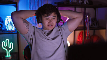 A relaxed asian man enjoys leisure time in a neon-lit gaming room at night.