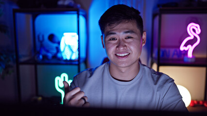 A young asian man smiling in a dark gaming room lit by colorful neon lights