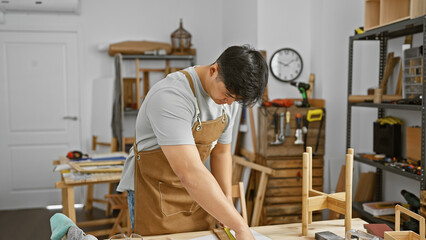 A young asian man measuring wood in a well-organized carpentry workshop.