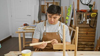 A focused asian man sanding wood in a well-organized carpentry workshop