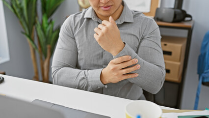 A young asian man experiencing wrist pain while working in a modern office setting
