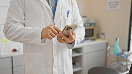 A young asian man in a lab coat texting on a smartphone inside a clinical laboratory.