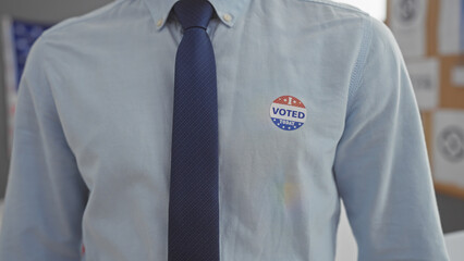 Close-up of a man wearing a 'voted' sticker with a tie, representing american civic duty in an election center.