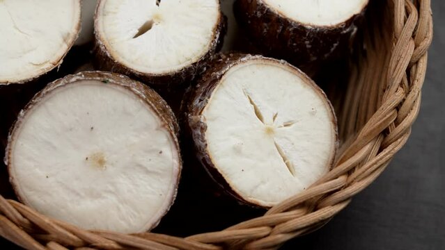 Organic sliced cassava root in wooden rattan bowl close up. Fresh Yucca tuber. Raw healthy food. Rotation