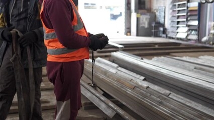 A worker moves large industrial metal parts using a remote control overhead rack crane. Heavy industry for manufacturing metal structures.
