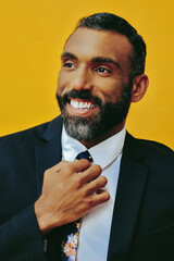 profile headshot of handsome positive smiling happy bearded man in suit with hand on tie, looking...