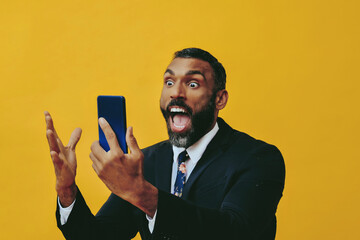 portrait of expressive angry excited bearded man in suit and tie with smartphone video call hand up yellow background