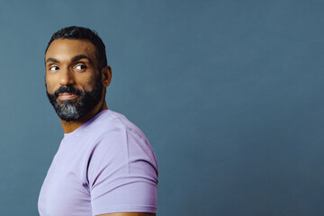 headshot portrait of a handsome smiling african american man with beard and mustache purple shirt on a gray looking away at copy space background