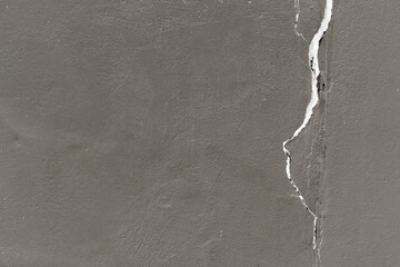 White vertical crack in a dark gray painted plastered stone wall