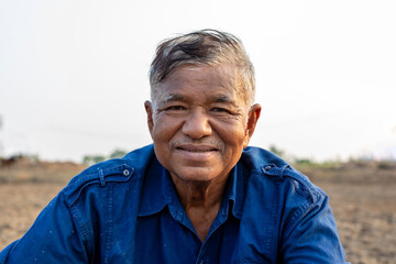 Portrait of elderly Asian man farmer wears blue shirt sitting on agricultural area and looking at...