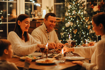 Happy family with kids enjoy Christmas dinner while sitting together at festive table in cozy home