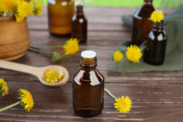 Fresh dandelion flowers and oil in a glass bottle on a wooden table. Flower essential oil. Green medicine, homeoparhy, hair and skin healthy care, detox therapy concept. Side view. 