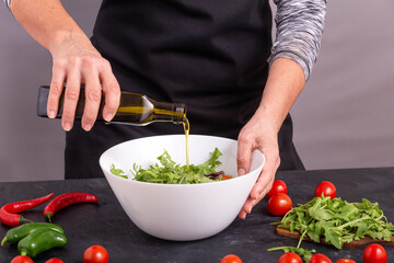A cook pouring olive oil on a fresh vegetable salad with tomatoes and arugula, closeup with selective focus