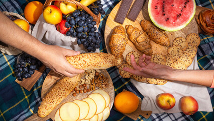 Top view of food laid out and the hands of people during a picnic, flat lay. The concept of summer outdoor recreation on the weekend