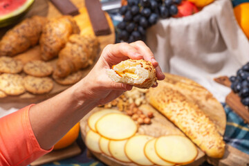 Close-up of hand holding bread with cheese against a background of laid out picnic food, selective focus. The concept of summer outdoor recreation on the weekend