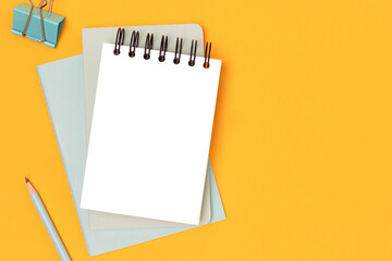 Workspace with empty notepad mockup and mint colored stationery on a yellow background. Office supplies.