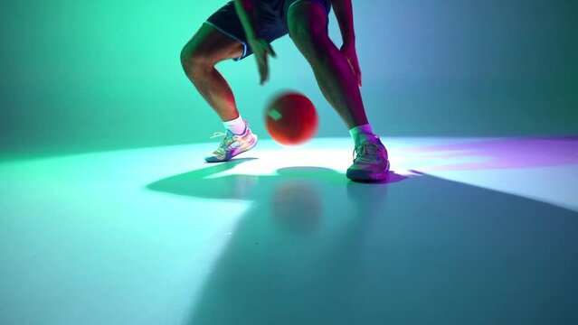 Jump by jump. Cropped image of male legs, basketball player in motion, showing skills in ball dribbling on gradient green, cyan background in neon. Concept of professional sport, competition, game