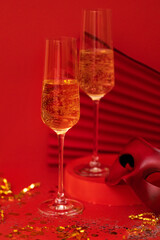 Two glasses of champagne on a podium. Carnival mask and paper fan on a bright red background