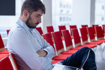 Portrait d'un homme qui travaille seul, assis dans une salle de réunion ou une salle de conférence avec un ordinateur portable. C'est un homme d'affaires ou un salarié d'une entreprise - 785374978