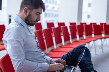 Portrait d'un homme qui travaille seul, assis dans une salle de réunion ou une salle de conférence avec un ordinateur portable. C'est un homme d'affaires ou un salarié d'une entreprise - 785374995