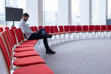 Portrait d'un homme qui travaille seul, assis dans une salle de réunion ou une salle de conférence avec un ordinateur portable. C'est un homme d'affaires ou un salarié d'une entreprise - obrazy, fototapety, plakaty