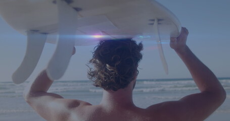 Image of lights over back view of caucasian surfer on beach