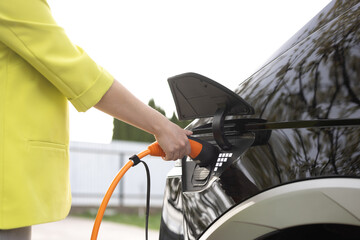 Woman opening the electric car's hatchet and plugging it in to charge. Close up shot of woman...