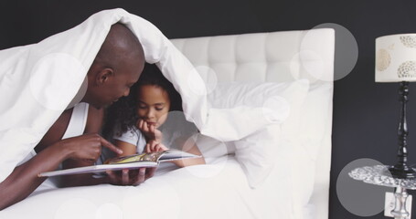 Image of light spots and trails over african american man and his daughter reading book together