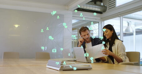 Image of connected computer icons forming globe over multiracial coworkers discussing in office