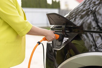 Female hand holding electric car plug for recharge plug in hybrid car at home or charging station. World Environment Day. Save world save life. Woman's hands plugging in her electric car to charge.