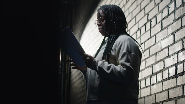 Lowkey shot of young Black female standup comedian reading her funny monologue while standing on dark stage under projector light at amateur theater