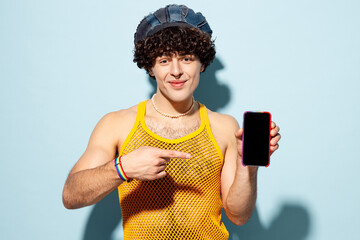 Young gay Latin man wear mesh tank top hat clothes hold use point on blank screen area mobile cell phone isolated on plain blue cyan background studio portrait. Pride day June month love LGBT concept. - 785388357