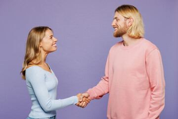 Side profile view young happy couple two friends family man woman wear pink blue casual clothes together do hand shake gesture greet each other isolated on pastel plain light purple background studio.