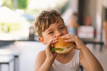 Little Boy Eating Sandwich and French Fries at Table. He appears focused on his meal, with a...