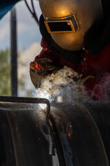 A welder wearing mask and eye protection, welding a pipeline. Industry worker welding