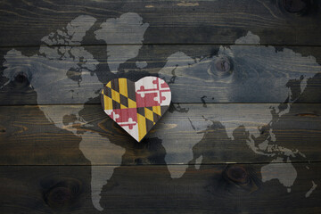 wooden heart with national flag of maryland state near world map on the wooden background.