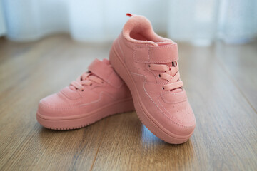 Child's pink sneakers on wooden floor. Cute girl's shoes on floor