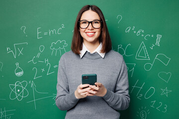 Young smiling smart teacher woman wear grey casual shirt glasses hold use mobile cell phone...