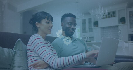 Image of social media icons over biracial couple smiling while using laptop together at home - Powered by Adobe