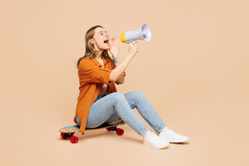 Full body young woman she wear orange shirt casual clothes sits on pennyboard skateboard scream in megaphone about hot news isolated on plain pastel light beige background studio. Lifestyle concept. - 785396591